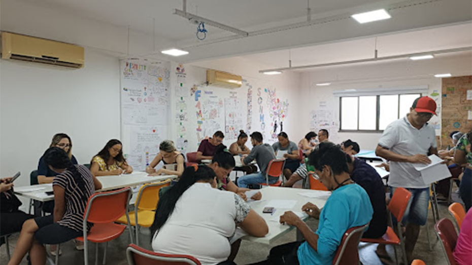 Foto de uma sala de convivência com um grupo de conviventes escrevendo cartas para o Projeto Intercâmbio literário.