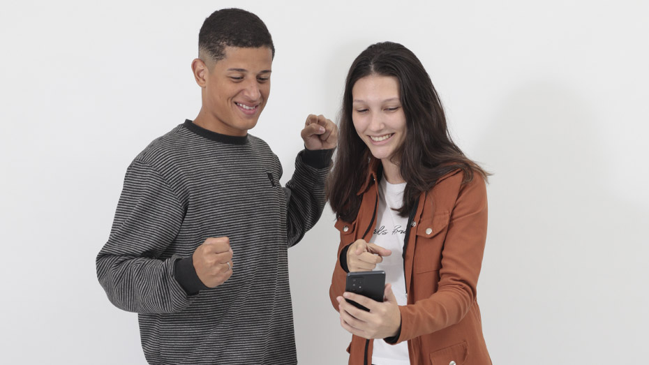 Imagem com fundo cinza e dois jovens felizes olhando para um celular fazendo gestos de comemoração por saber que o CIEE tem uma plataforma de cursos gratuitos e on-line.